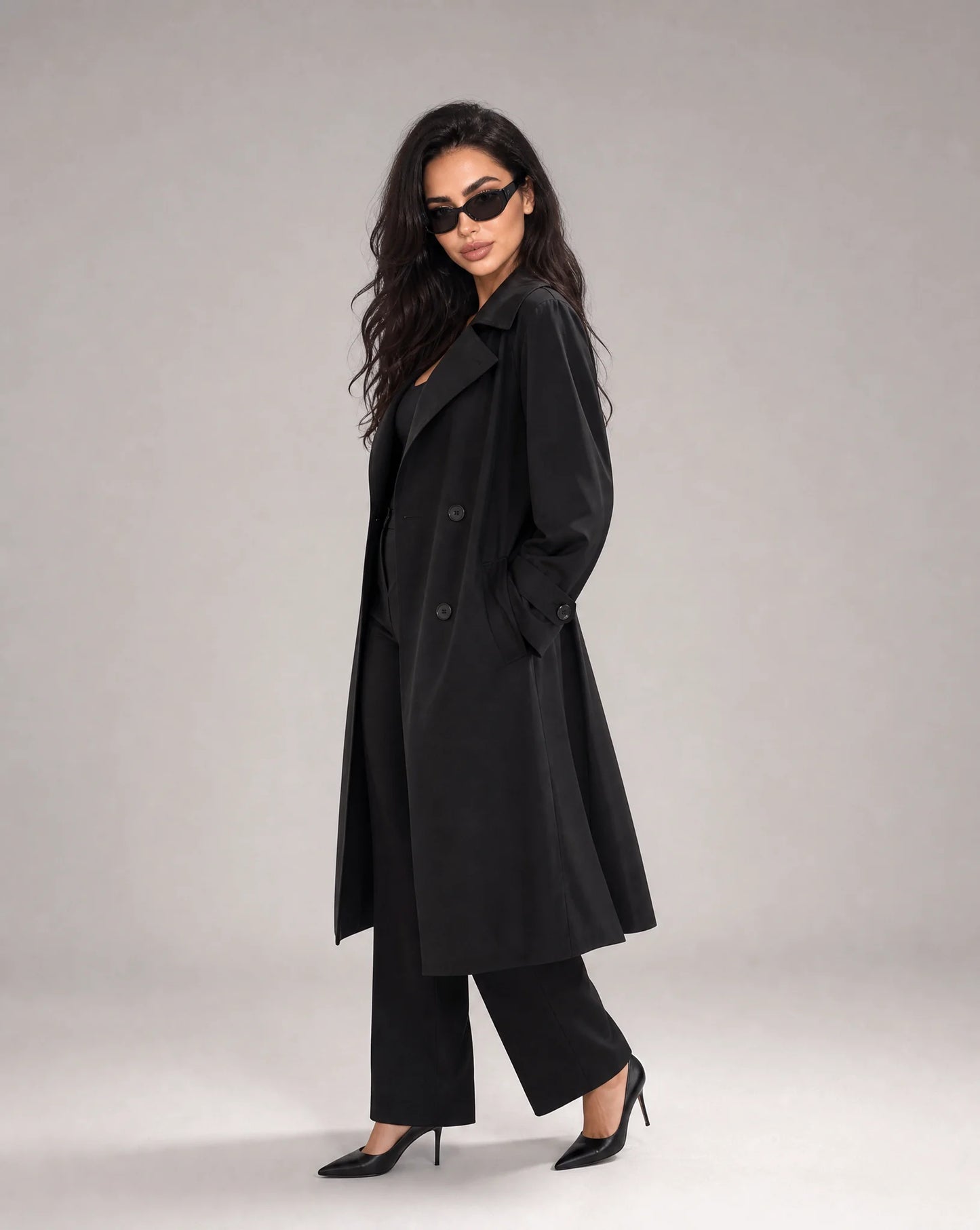 Woman wearing ILYNORA black long trench coat with classic double-breasted styling and sophisticated relaxed fit