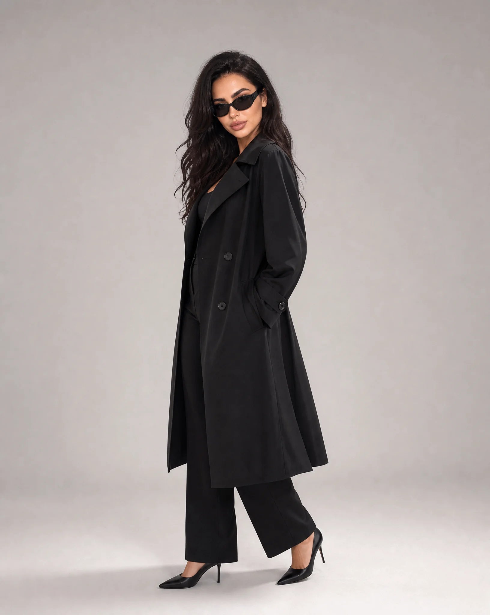 Woman wearing ILYNORA black long trench coat with classic double-breasted styling and sophisticated relaxed fit