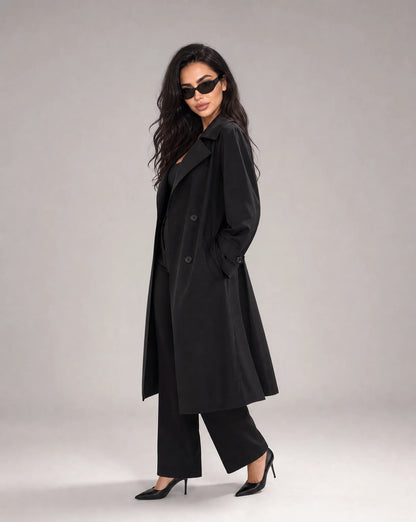 Woman wearing ILYNORA black long trench coat with classic double-breasted styling and sophisticated relaxed fit