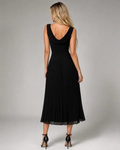 Back view of women's black draped cowl neck pleated midi dress with flowing pleated skirt and timeless formal styling by ILYNORA