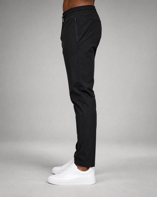 Men's black technical jogger pants with slim tapered fit, stretch fabric and side profile by ILYNORA
