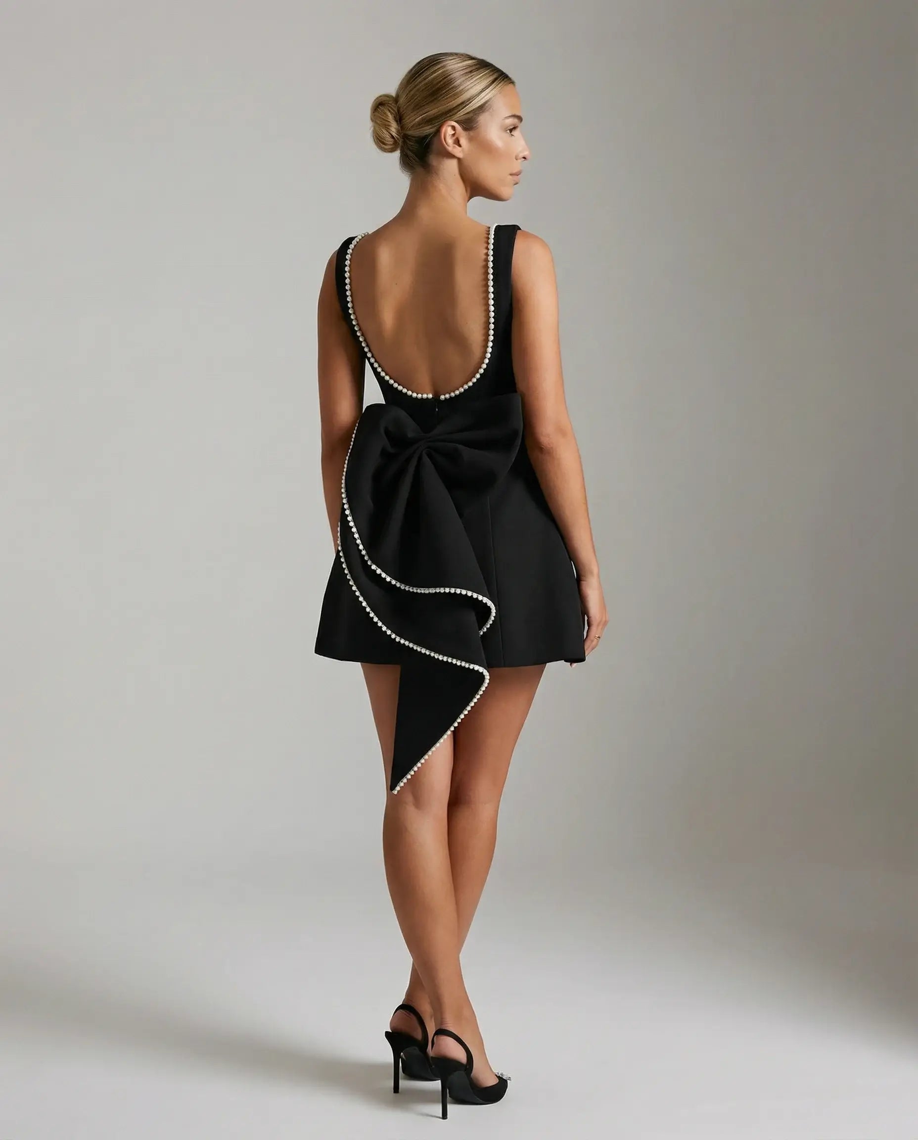 Black A-line mini dress with pearl trim by Ilynora, back view showing open back and statement bow