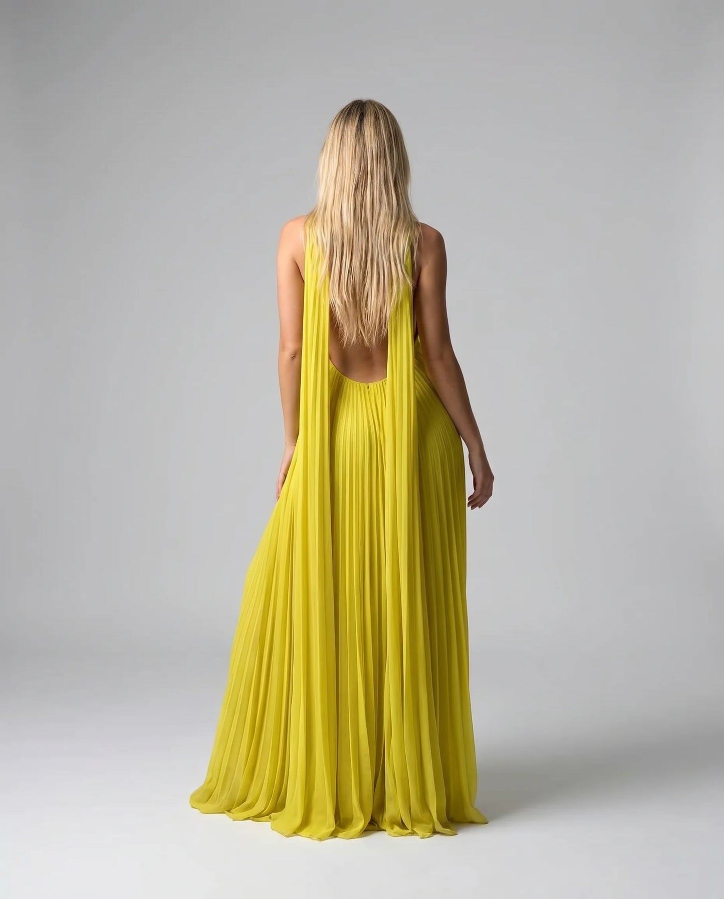 Back view of a yellow pleated halter maxi dress with open back and floor length silhouette