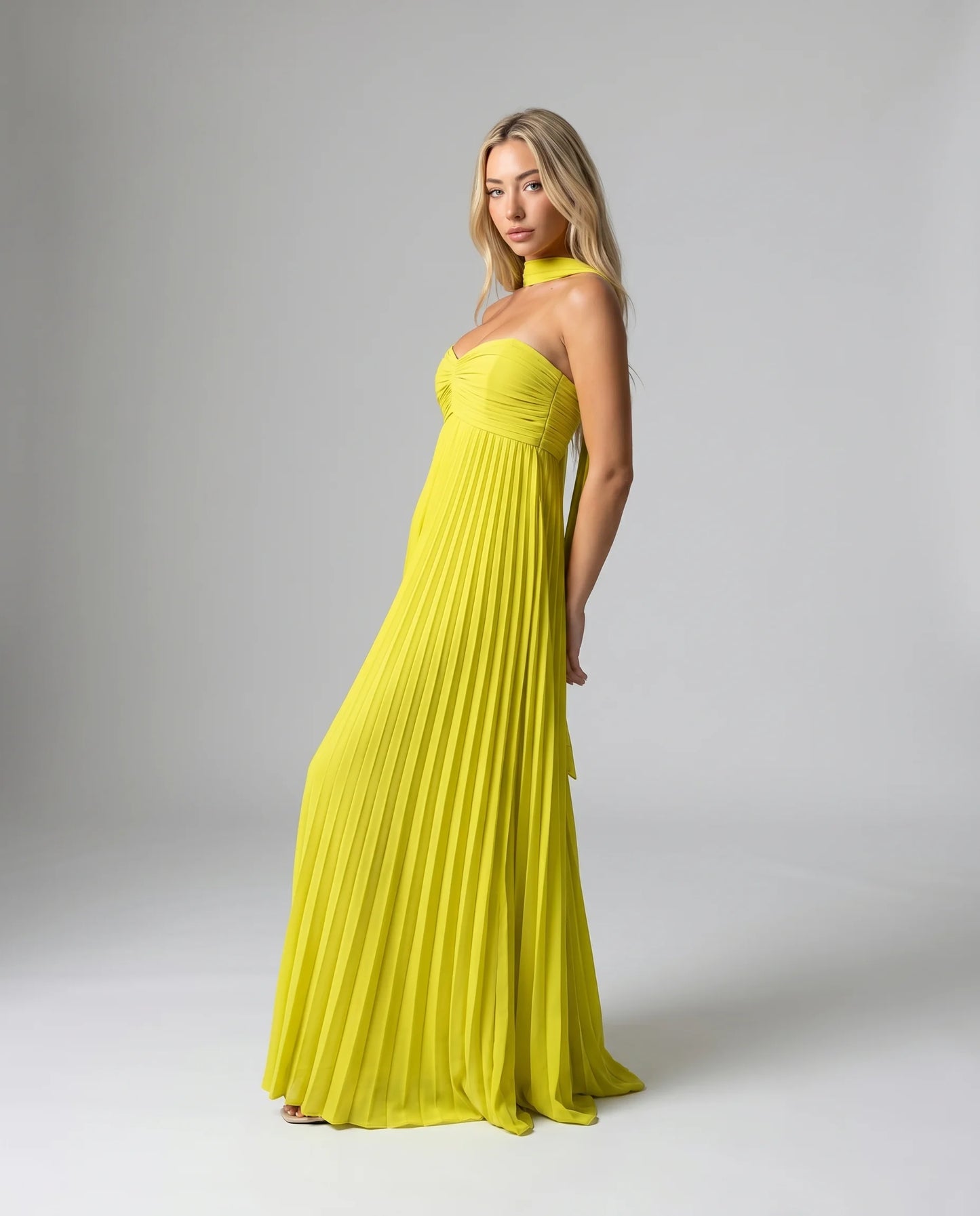 Side view of a yellow pleated halter maxi dress with elegant drape and flowing pleated skirt