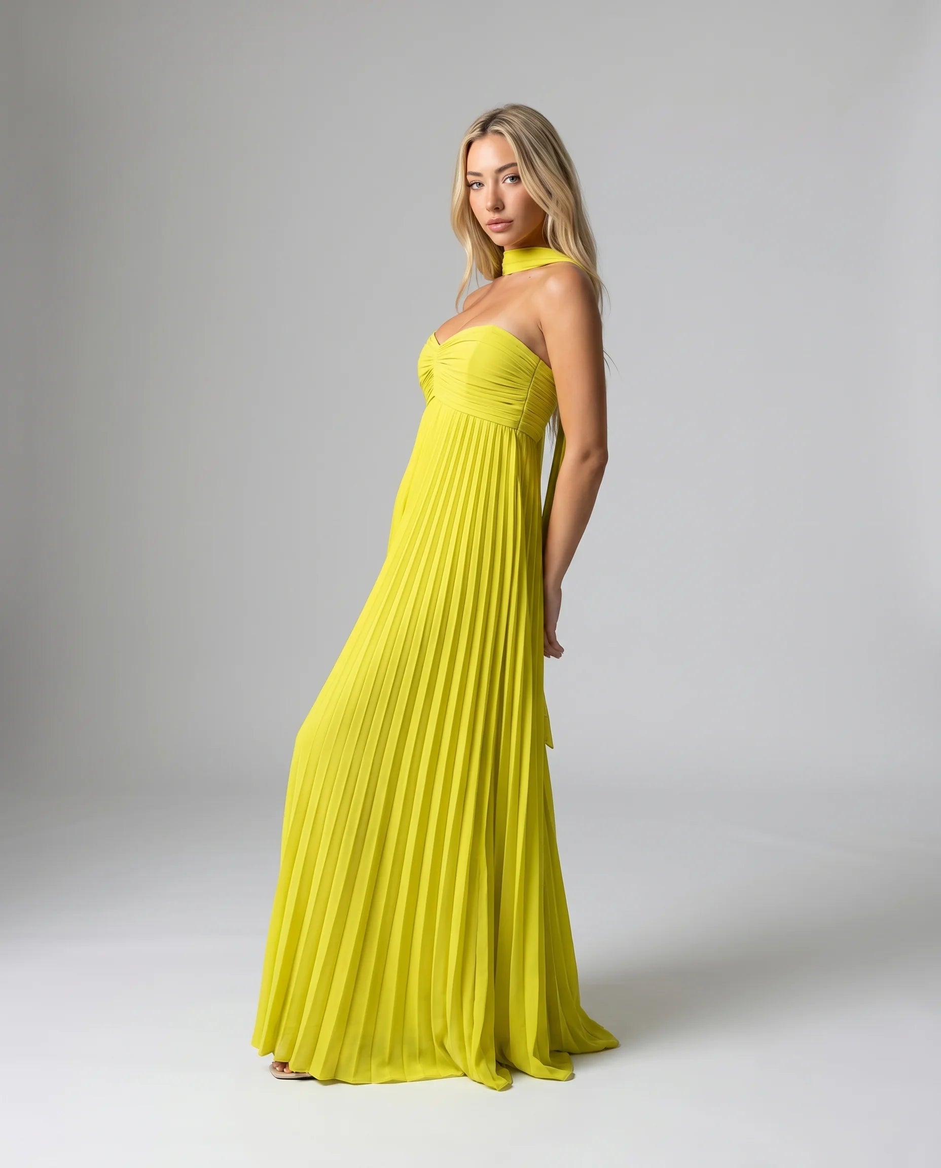 Side view of a yellow pleated halter maxi dress with elegant drape and flowing pleated skirt