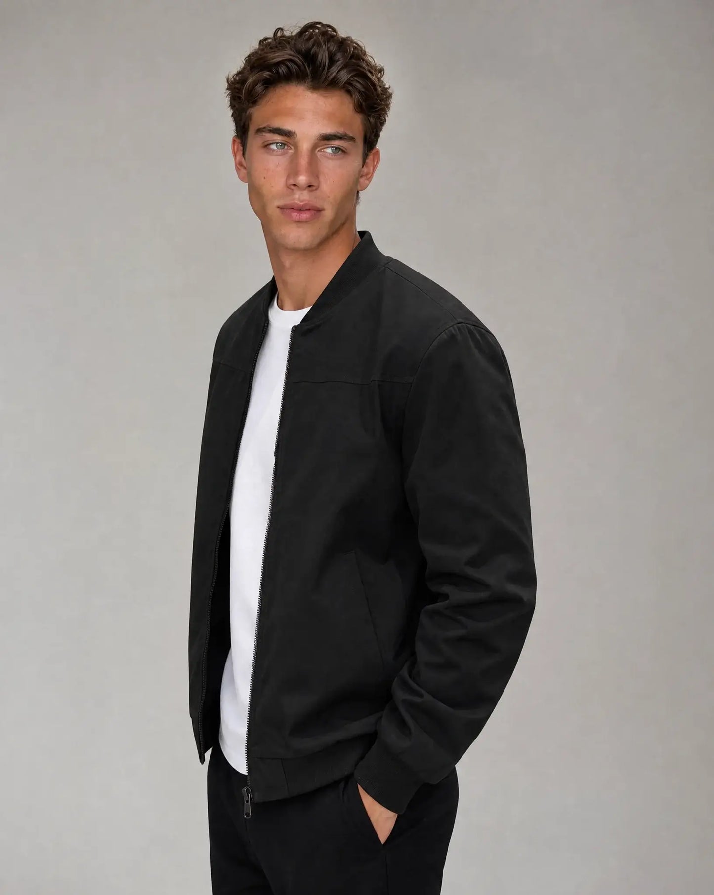 Black zip up bomber jacket for men by Ilynora, angled view highlighting ribbed collar and structured silhouette