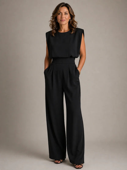 Women's black sleeveless pleated wide leg jumpsuit with draped bodice, tailored waist and sophisticated evening silhouette by ILYNORA