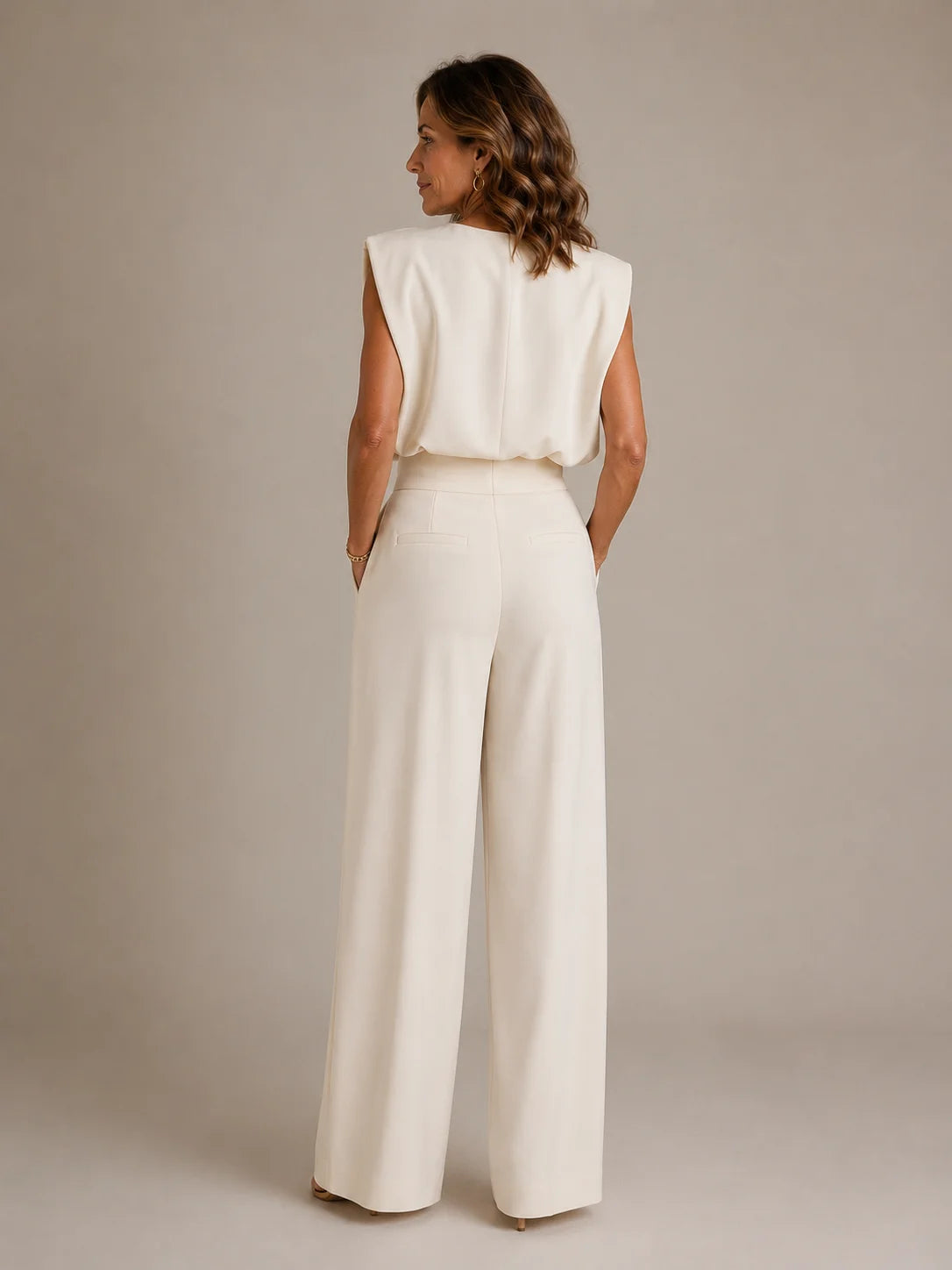 Back view of women's golden sleeveless pleated wide leg jumpsuit with elegant draped fit and flowing full length trousers by ILYNORA