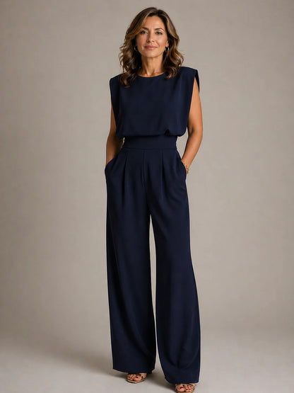 Women's navy sleeveless pleated wide leg jumpsuit with elegant draped bodice, tailored waist and flowing evening silhouette by ILYNORA