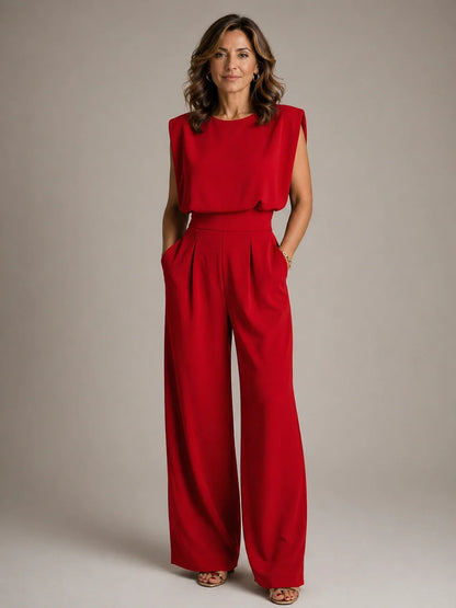 Women's red sleeveless pleated wide leg jumpsuit with flowing trousers, draped bodice and elegant formal occasion styling by ILYNORA